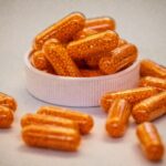 비타민과 영양제: “다 먹어야 할까?” 운동인이 꼭 챙겨야 할 필수 영양소 Top 3 Orange capsules filled with small beads spill from container.