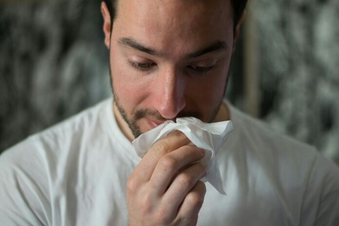 sick man blowing nose into tissue
