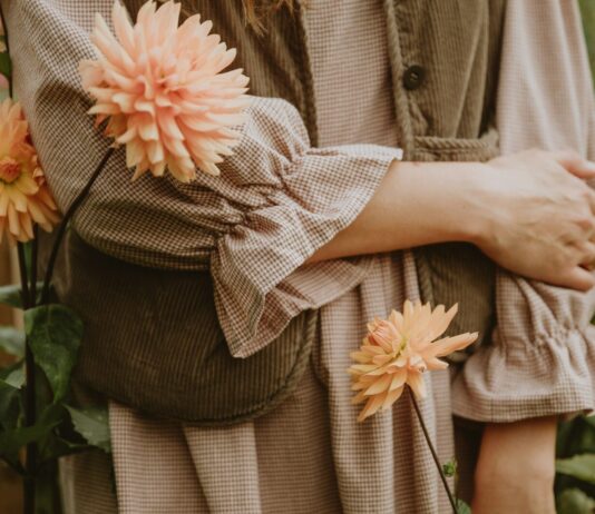 집에서도 실천 가능한 ‘마음 챙김’ 루틴, 스트레스 시대의 건강 관리법 A person in a brown gingham dress and corduroy vest among peach dahlias